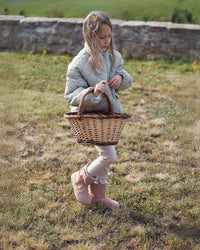Lifestyle fotografija barefoot cizama Siberia roze dete stoji na travi sa korpom