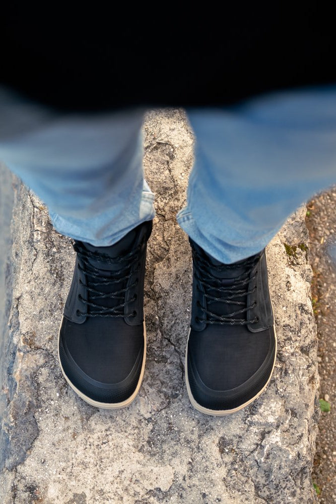 Arctic Edge crne barefoot čizme odozgo na nogama osoba stoji na kamenu