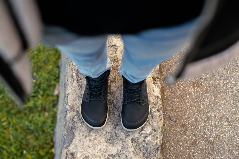 Arctic Edge crne barefoot čizme odozgo na nogama osoba stoji na kamenu