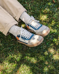 Lifestyle fotografija barefoot patika Majorca Teal prikaz na nozi dok osoba sedi na travi