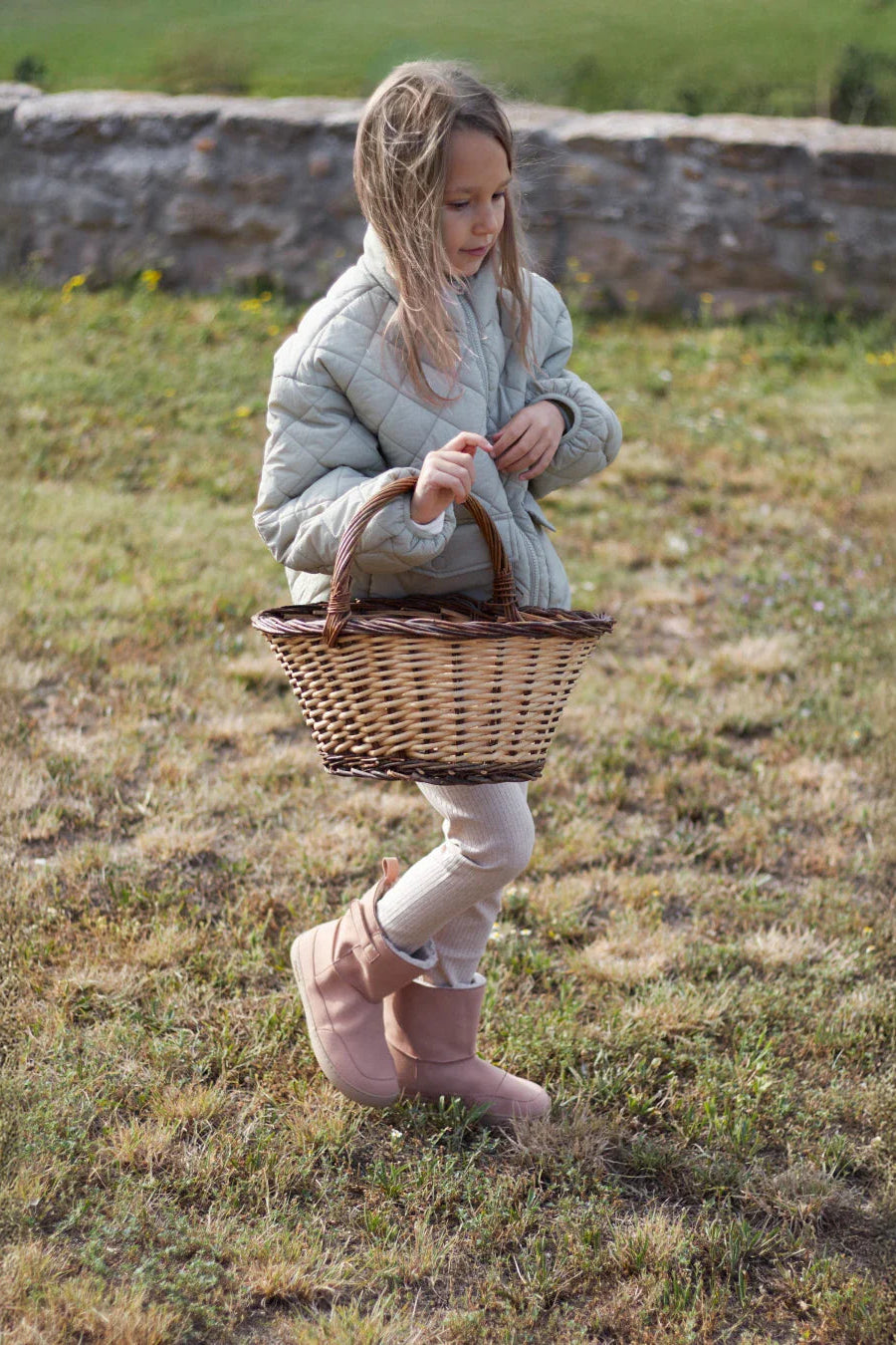 Lifestyle fotografija barefoot cizama Siberia roze dete stoji na travi sa korpom