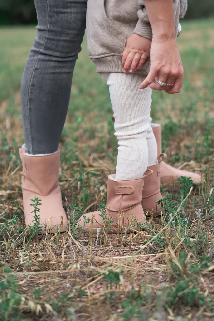 Lifestyle fotografija barefoot cizama Siberia roze dete stoji na travi pored odrasle osobe